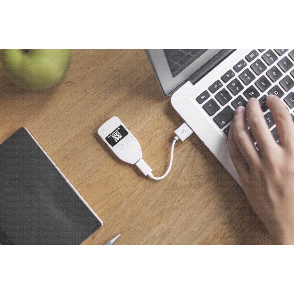 Trezor Model One — white device connected by a cable to a laptop on a wooden desk