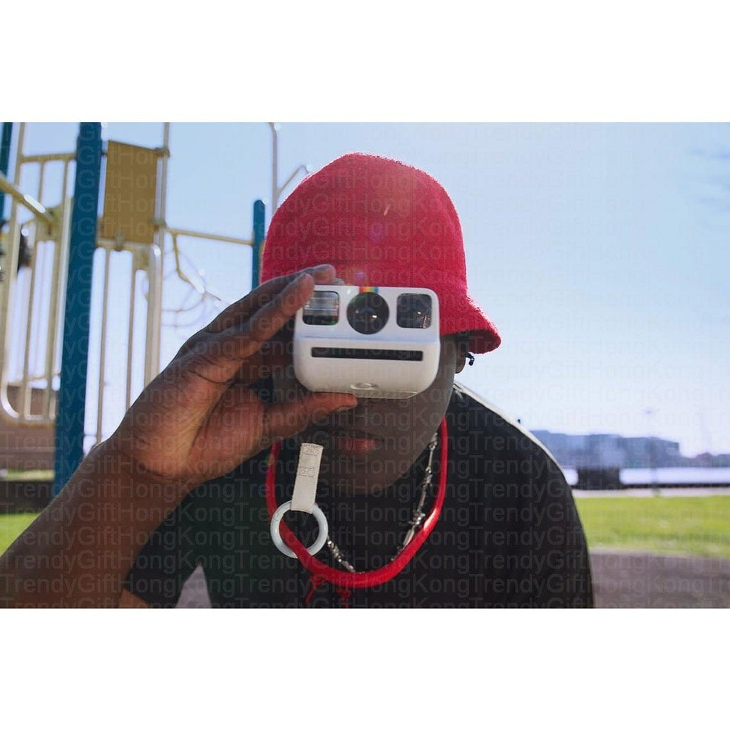 Person wearing a red hat holds a white camera up to their face outdoors.