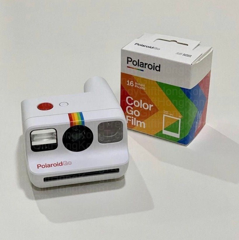 White camera beside a Color Go Film box on a light surface, photographed from above.